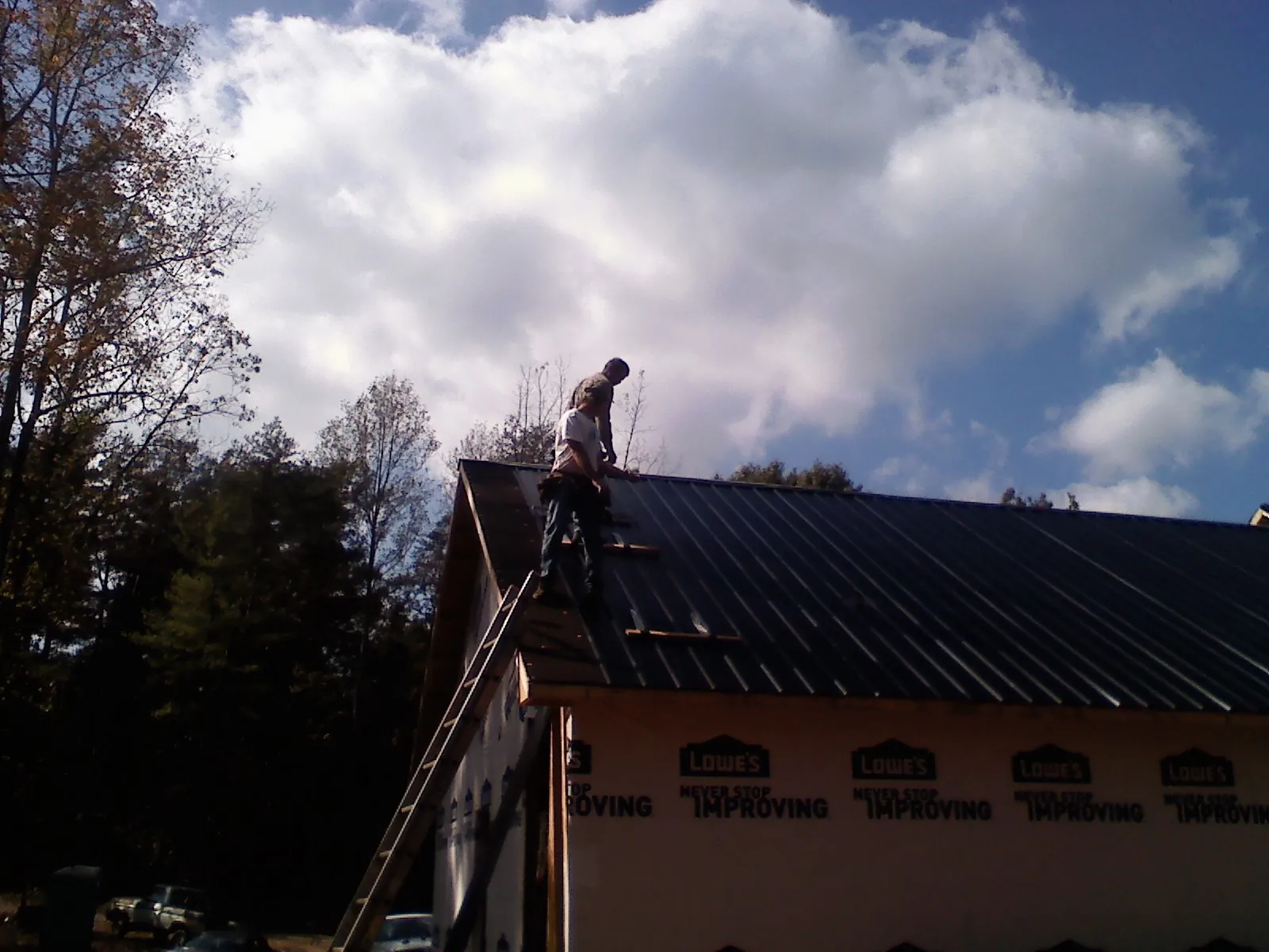 Roofer fastening dark metal panels high against a cloudy sky, from a Roof Inspection job in Erlanger
